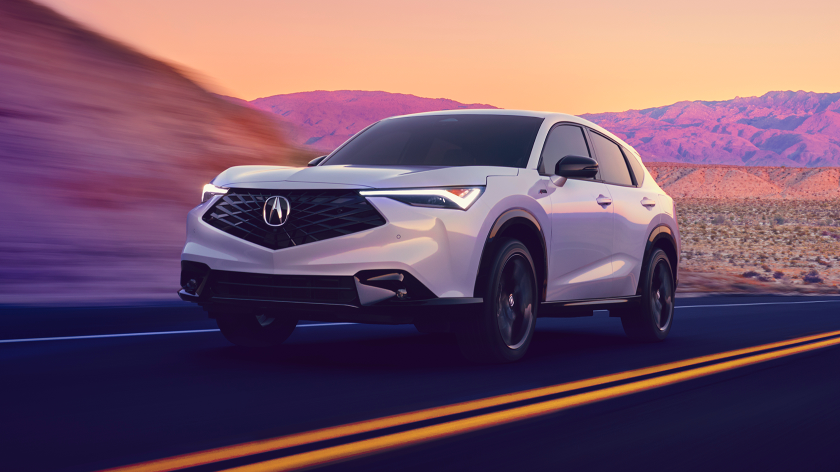 Acura ADX gris vu de face sur une route avec des montagnes colorées de violet en arrière-plan. 