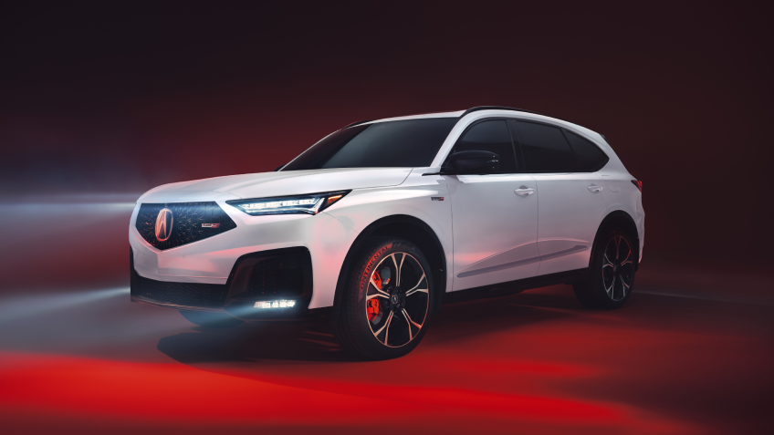 3/4 side front view of white MDX, with its headlights on, in a studio lit with red light.