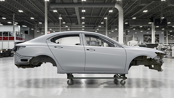 Passenger side view of a white vehicle frame hoisted on a dolly inside the Acura Performance Manufacturing Centre	Vue du côté passager d’un cadre de véhicule blanc sur un chariot à l’intérieur du Performance Manufacturing Centre d’Acura.